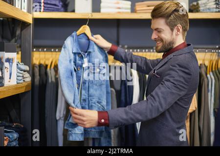 Jeder braucht eine klassische Denim-Jacke im Schrank. Aufnahme eines jungen Mannes, der in einer Boutique Kleidung ansieht. Stockfoto
