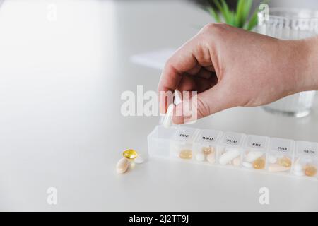 Nahaufnahme von weiblichen älteren Händen, die Pillen sortieren. Medizinische Pille Box mit Dosen von Tabletten für die tägliche Einnahme mit weißen, gelben, beigen Drogen und Kapseln. Junge Frau bekommt ihre täglichen Vitamine zu Hause Stockfoto