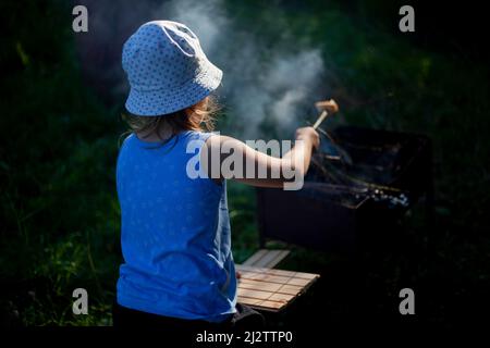 Kind beim Picknick. Mädchen backt Brot auf Stock. Sommer Erholung im Freien. Kind in der Nähe des Feuers. Kind in panama. Das Mädchen hält einen Stock Brot über dem Feuer. Stockfoto