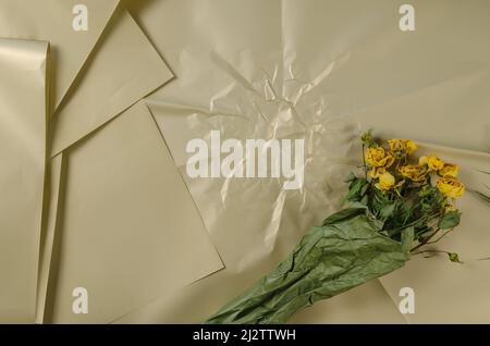 Ein Bouquet aus welkenden Blumen auf beigem Hintergrund. Getrocknete gelbe Rosen in grünem Papier verpackt. Stockfoto