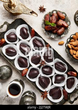 Schwarzer türkischer Kaffee mit Gewürzen in orientalischen kleinen Tassen und gesunden zuckerfreien hausgemachten Rohkost vegane Schokolade Bonbons mit getrockneten datierten und Mandeln auf Be Stockfoto