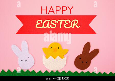 Frohe Ostern. Schneiden Sie die Filzapplikationen von weißen und braunen Kaninchen und das Huhn, das aus dem Ei geschlüpft ist, heraus. Rosa Hintergrund. Flach liegend. Stockfoto