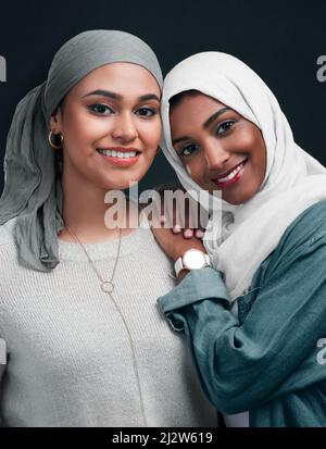 Freunde bis zum Ende. Kurzer Schuss von zwei attraktiven jungen Frauen, die Hijabs tragen und dicht beieinander vor schwarzem Hintergrund im Studio stehen. Stockfoto