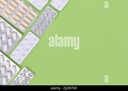 Verschiedene Kapseln und Pillen in Blisterpackungen auf der rechten Seite des grünen Hintergrundes mit Kopierraum Stockfoto