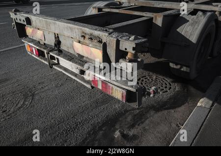 Rückenteil mit Rücklicht eines leeren LKW-Ladewagens, der auf dunkler Asphaltstraße steht Stockfoto