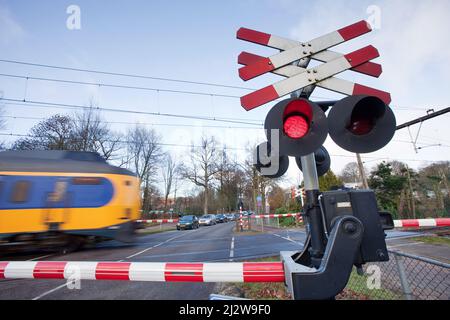 Niederlande, Zug passiert einen Bahnübergang in Arnhem mit Kreuzböcken, roten Lichtern, elektrischen Glocken und Halb-Barriere-Toren. Stockfoto