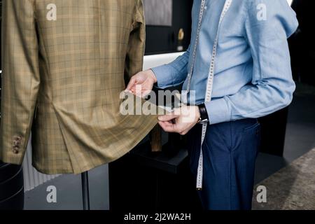 Ein Schneidermann mit einem Maßband inspiziert einen fertigen Anzug in der Werkstatt Stockfoto