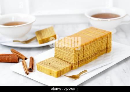 Indonesische Tausendschicht-Torte oder Lapis Legit. Wird normalerweise auf Lebaran, Natal und Imlek serviert. Serviert mit Tee, Backwarenkonzept mit weißem Hintergrund Stockfoto