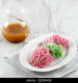 Putu Mayang oder Petulo, indonesischer traditioneller javanischer Snack aus Reismehlsträngen, zusammengerollt zu einem Ball mit Lebensmittelfarbe, serviert mit Kokosnuss Stockfoto