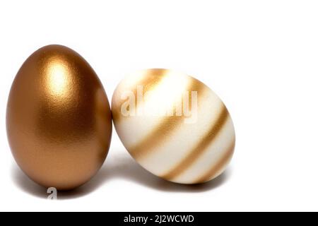 Nahaufnahme von zwei Ostereiern ein ganz Gold neben einem mit Linien auf weißem Hintergrund als Konzept von Wohlstand und Reichtum verziert Stockfoto