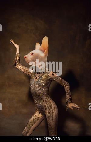 Flexible anmutige weibliche Modell wie mittelalterliche Person in Vintage-Kleidung von Katzenkopf auf dunklen Retro-Hintergrund isoliert geführt. Konzept des Vergleichs von Stockfoto