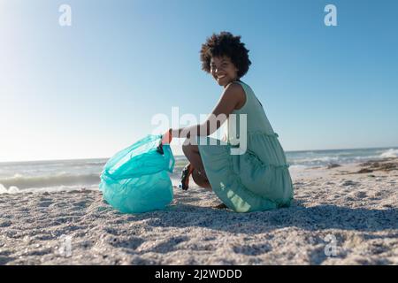 Seitenansicht Porträt eines lächelnden afroamerikaners, der beim Sammeln von Abfällen mit einem Plastikbeutel hocke Stockfoto