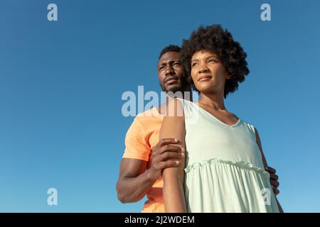 Low-Angle-Ansicht des afroamerikanischen Paares, das vor einem klaren blauen Himmel mit Kopierraum steht Stockfoto