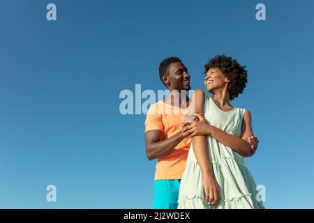 Low-Angle-Ansicht des lächelnden afroamerikanischen Paares vor klarem blauen Himmel mit Kopierraum Stockfoto