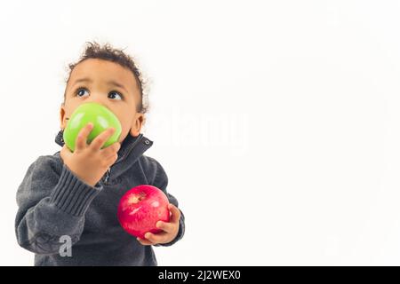 Kleiner afroamerikanischer gewellter Junge, der nach oben schaute und große grüne und rote Äpfel hielt, Studio schoss weißen Hintergrund mittlerer Nahaufnahme Kopierraum. Hochwertige Fotos Stockfoto