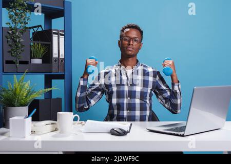 Aktive selbstbewusste und starke junge Erwachsene Hanteln heben, um in Form zu bleiben, während der Arbeit im Büro. Fit und sportlich Mann macht Fitness-Training Übung für steife Muskeln. Stockfoto