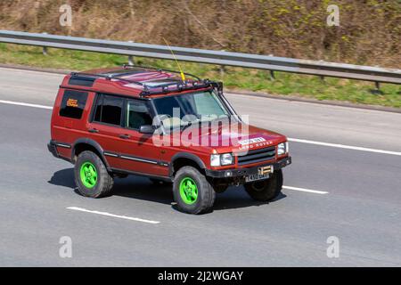 1999 90s Neunzigs Red Land Rover Discovery TD5 GS 5STR 2495cc 4-Gang-Automatik mit grünen Rädern lackierte Felgen und erhöhte Aufhängung; Fahren auf der Autobahn M61, Großbritannien Stockfoto