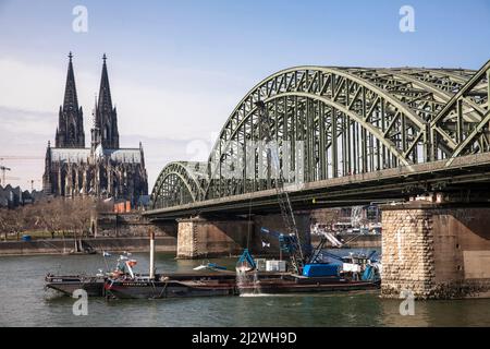 Bagger auf einem Schiff vertieft das Flussbett des Rheins unter der Hohenzollernbrücke, dem Dom, Köln, Deutschland. Bagger auf einem Schiff Stockfoto