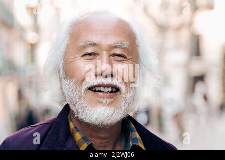 Älterer asiatischer Mann lächelt vor der Kamera im Freien - Fokus auf männliche Augen Stockfoto