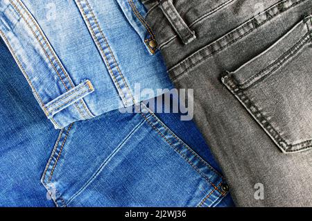 Hintergrund mit Denim-Struktur. Stapel verschiedener Jeans aus Baumwolle mit Taschen und Saum mit orangefarbenen Fadenstichen, Draufsicht. Stockfoto