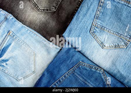 Hintergrund aus einer Vielzahl von Jeans. Jeans aus Baumwolle mit Taschen und Saum mit orangefarbenen Fadenstichen, Draufsicht. Stockfoto