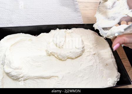 Eine Frau gießt den gemischten Quark und die Schlagsahne in einen gebackenen Kakaokuchen auf einem Backblech Stockfoto