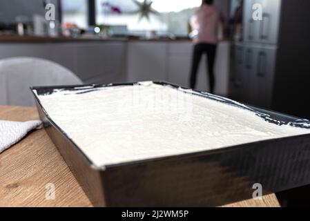 Gemischter Quark mit Schlagsahne auf einem gebackenen Kakaoteig auf einem Backblech, auf dem Tisch liegend. Stockfoto