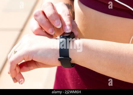 Nahaufnahme des Handgelenks eines sportlichen Mädchens mit einem intelligenten Tracker, den sie mit dem Zeigefinger ihrer rechten Hand berührt. Stockfoto