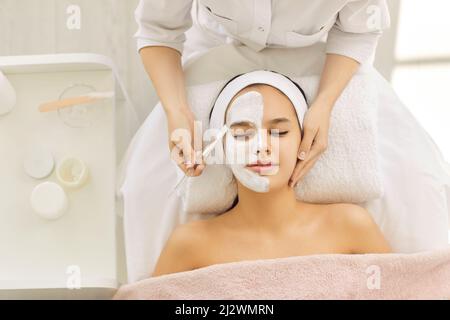 Zufriedene junge schöne Frau nutzt Dienstleistungen der professionellen Kosmetikerin im Schönheitssalon oder Spa. Stockfoto