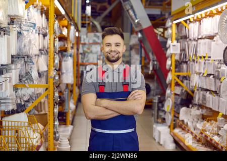 Verkäufer in Uniform im Baumarkt. Mann, der neben den Regalen mit Werkzeugen stand und lächelte Stockfoto