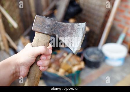 Mann mit Axt. Axt in der Hand. Ein starker Mann hält eine Axt in den Händen vor dem Hintergrund von Feuerholz. Selektiver Fokus, unscharfer Hintergrund Stockfoto