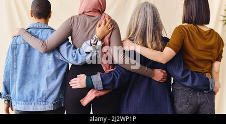 Rückansicht des Internationalen Frauentags Porträt von vier Frauen, die solidarisch mit den Armen umeinander stehen Stockfoto