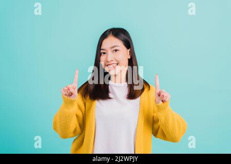 Portrait Asian schöne junge glückliche Frau Teen lächelnd zeigen weiße Zähne Sie zeigt den Finger bis zu leeren Raum Studio auf blauem Hintergrund gedreht Stockfoto