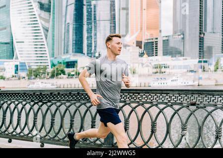 Junger Athlet Mann Läufer läuft am Sommermorgen, Hintergrund Stadt Straße. Sporttraining. Fitness Cardio-Training an der frischen Luft, Joggen Stockfoto