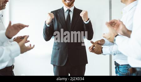 Der Leiter des Unternehmens, umgeben von Mitarbeitern, die ihm applaudieren, freut sich über den Erfolg Stockfoto