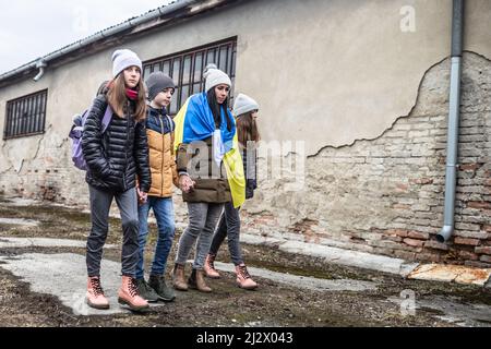 Frau hält die ukrainische Flagge, als sie mit drei Kindern in einer verwelkten Umgebung vor dem Konflikt mit Russland flieht. Stockfoto