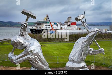 Port Glasgow, Schottland, Vereinigtes Königreich. 4.. April 2022. Die Fähre MV Glen Sannox wird von der neuen Skulptur Shipbuilders of Port Glasgow von John McKenna eingerahmt. Die umstrittene Fähre wird derzeit auf der Ferguson Marine Werft in Port Glasgow gebaut. Der Vertrag über den Bau von zwei Fähren wird voraussichtlich Gegenstand einer Untersuchung des parlamentarischen Ausschusses im schottischen Parlament sein. Iain Masterton/Alamy Live News Stockfoto