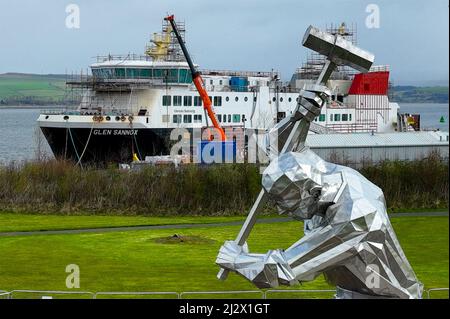 Port Glasgow, Schottland, Vereinigtes Königreich. 4.. April 2022. Die Fähre MV Glen Sannox wird von der neuen Skulptur Shipbuilders of Port Glasgow von John McKenna eingerahmt. Die umstrittene Fähre wird derzeit auf der Ferguson Marine Werft in Port Glasgow gebaut. Der Vertrag über den Bau von zwei Fähren wird voraussichtlich Gegenstand einer Untersuchung des parlamentarischen Ausschusses im schottischen Parlament sein. Iain Masterton/Alamy Live News Stockfoto