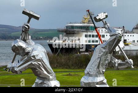 Port Glasgow, Schottland, Vereinigtes Königreich. 4.. April 2022. Die Fähre MV Glen Sannox wird von der neuen Skulptur Shipbuilders of Port Glasgow von John McKenna eingerahmt. Die umstrittene Fähre wird derzeit auf der Ferguson Marine Werft in Port Glasgow gebaut. Der Vertrag über den Bau von zwei Fähren wird voraussichtlich Gegenstand einer Untersuchung des parlamentarischen Ausschusses im schottischen Parlament sein. Iain Masterton/Alamy Live News Stockfoto