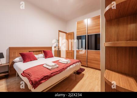 Schlafzimmer mit Kingsize-Bett, Holzmöbeln, Kleiderschrank mit Schiebetür und passenden Regalen Stockfoto