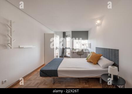 Schlafzimmer mit Kingsize-Bett, runden Nachttischen aus Holz, weißen Holzschreibtischen unter dem Fenster und passendem weißen Holzschrank Stockfoto