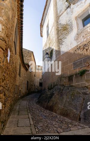 Caceres, Spanien - 30. März 2022: Schmale Fußgängerstraße mit Kopfsteinpflaster, die durch die historischen alten Gebäude in der Altstadt von Cacere führt Stockfoto