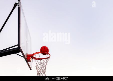 Ball, der in einen Basketballkorb mit dem Himmel im Hintergrund eintritt, Konzept des urbanen Sports im Freien, Platz für Text kopieren Stockfoto