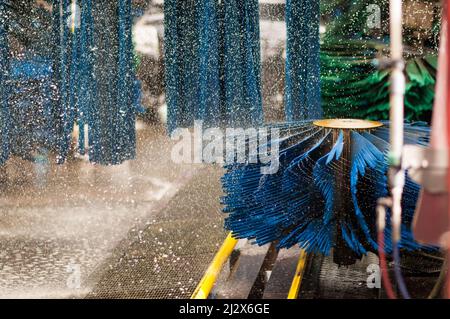 Schuss während der Vorbereitung einer automatischen Autowaschmaschine. Die Waschbürsten drückten Wasser über den ganzen Platz. Stockfoto