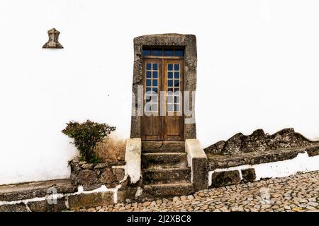 Santa Maria de Marvao, Portugal - 30. März 2022: Weiß getünchte Hausfront mit alter Holztür in Steinrahmen auf einer gepflasterten Straße Stockfoto