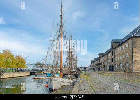 Segelboote mit Masten stehen auf dem Wasser des Kanals in der Nähe von dreistöckigen Gebäuden aus grauen Ziegeln auf einer Straße mit einem Steinpflaster Christianshavn.C Stockfoto