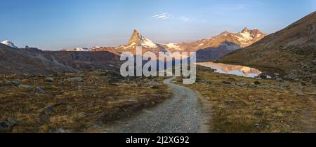 Ein Wanderweg, der von Fluhalp in Richtung Stellisee mit dem Matterhorn hinunterführt, in den Tagen letztes Licht in der Ferne. Wallis. Schweiz Stockfoto