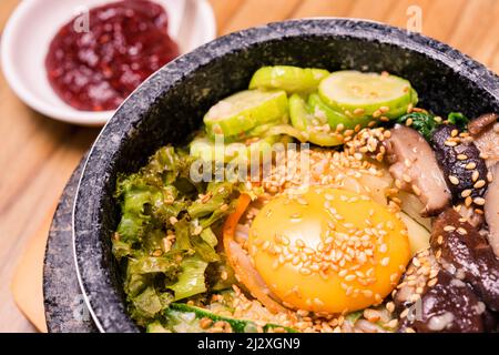 Bibimbap in einer schwarzen, beheizten Steinschüssel, koreanisches traditionelles Gericht - Bibimbap gemischter Reis mit Gemüse umfassen Rindfleisch und Spiegelei, japanisches Hot Pot Essen Stockfoto