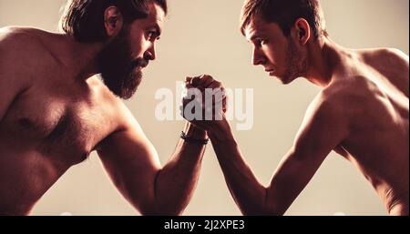 Stark muskulös bärtiger Mann, der einen schwach schwachen Mann am Arm kämpft. Arme ringen dünne Hand, großer starker Arm im Studio. Zwei Männerhände umklammten Arm-Wrestling Stockfoto