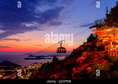 Eine Seilbahn nähert sich der oberen Station auf dem SRD-Berg, Dubrovnik, Kroatien, während die Sonne dahinter untergeht. Passagiere können in der Seilbahn gesehen werden. Stockfoto